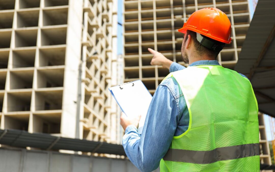 Ingeniero supervisando construcción de edificio con casco naranja y chaleco de seguridad.